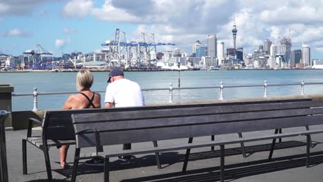 slowmo - older couple sitting on bench in devonport harbour and looking at auckland skyline, new zealand