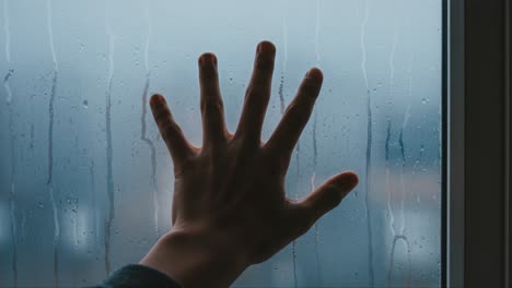 a hand pressed against a rain-drenched window, capturing the essence of isolation and reflection amidst the melancholic atmosphere of a gloomy day
