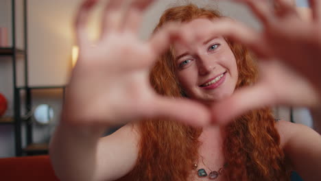 redhead young woman makes symbol of love, showing heart sign to camera, express romantic feelings