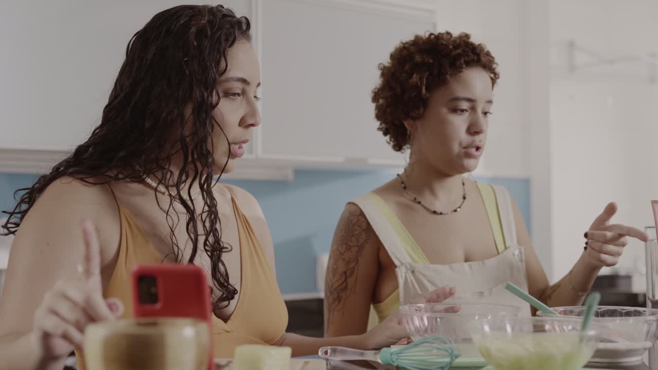 Two women cooking and preparing food in a kitchen, possibly recording an online tutorial