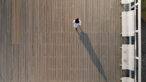 Birds-Eye-View-Of-Women-In-White-Dress-Walking-Across-Wooden-Pier