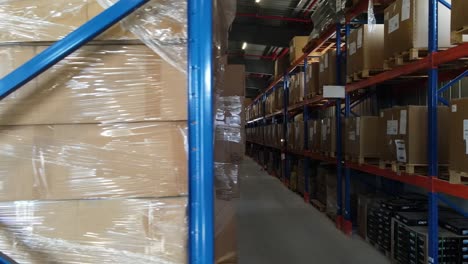 cardboard boxes wrapped in plastic film are stored on metal shelves in a warehouse with a visible fire extinguisher