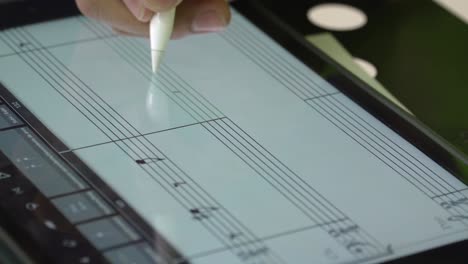 man meticulously crafts musical compositions using digital sheet music software on a tablet