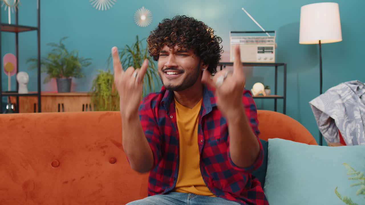Overjoyed young indian man showing rock n roll gesture cool sign dancing rejoicing in success