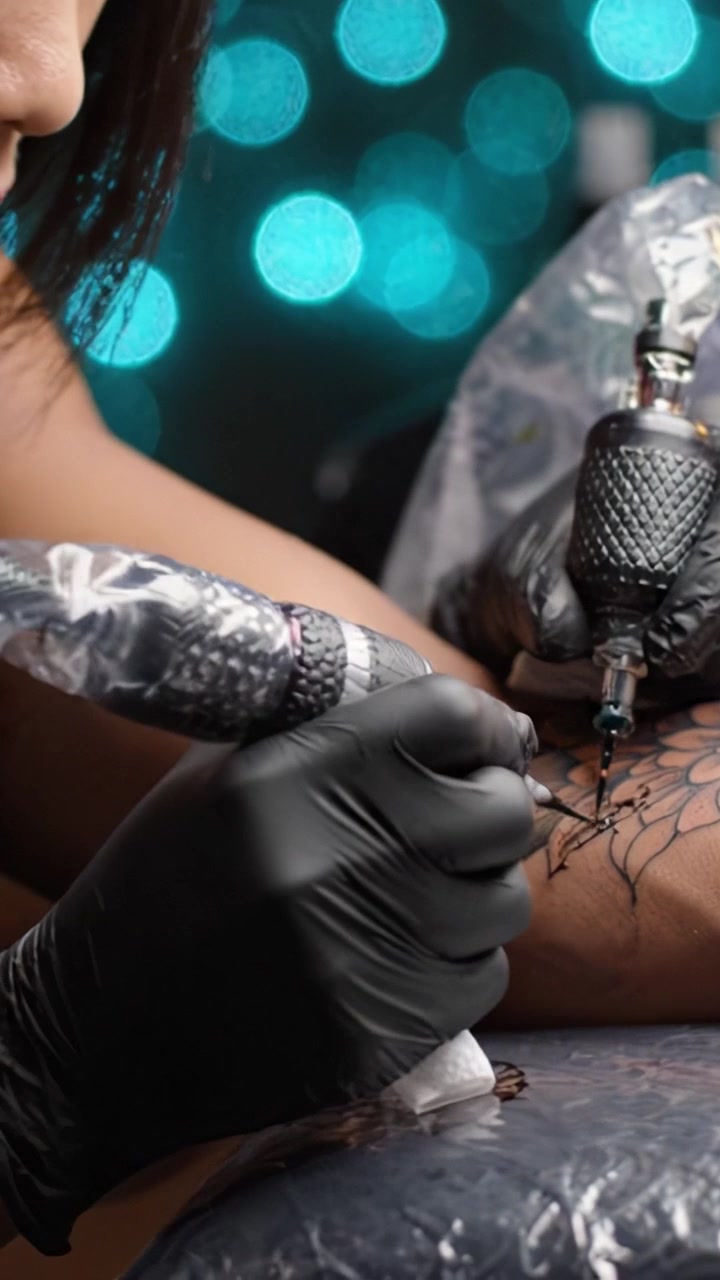 L'arte nell'inchiostro: Un abile tatuatore lavora delicatamente su un disegno floreale con strumenti di precisione su uno sfondo sfocato e abbagliante.