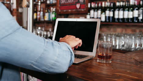 Mann-Benutzt-Laptop,-Während-Er-Whiskey-An-Der-Theke-Trinkt