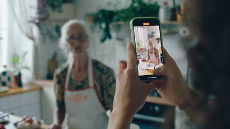 boy holding phone and filming grandmother explaining cooking recipe in kitchen