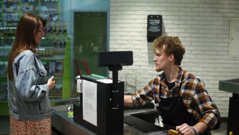 supermarket: checkout counter. female customer pays with smartphone for her food items, applying mobile on wireless terminal