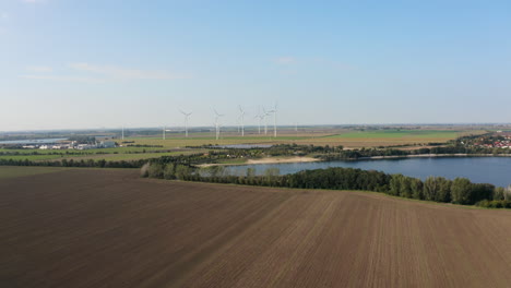 Paisaje-Soleado-Con-Campos,-Lago-Y-Molinos-De-Viento-Moviendo-Imágenes-De-Drones-4k