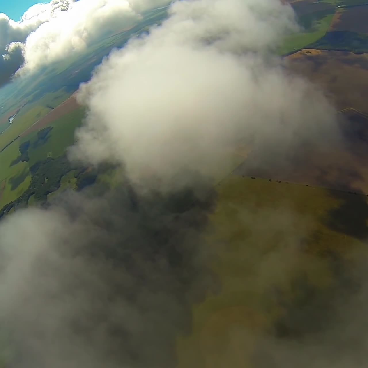Soaring in the air among the white clouds. Hands holding the straps of black and orange parachute