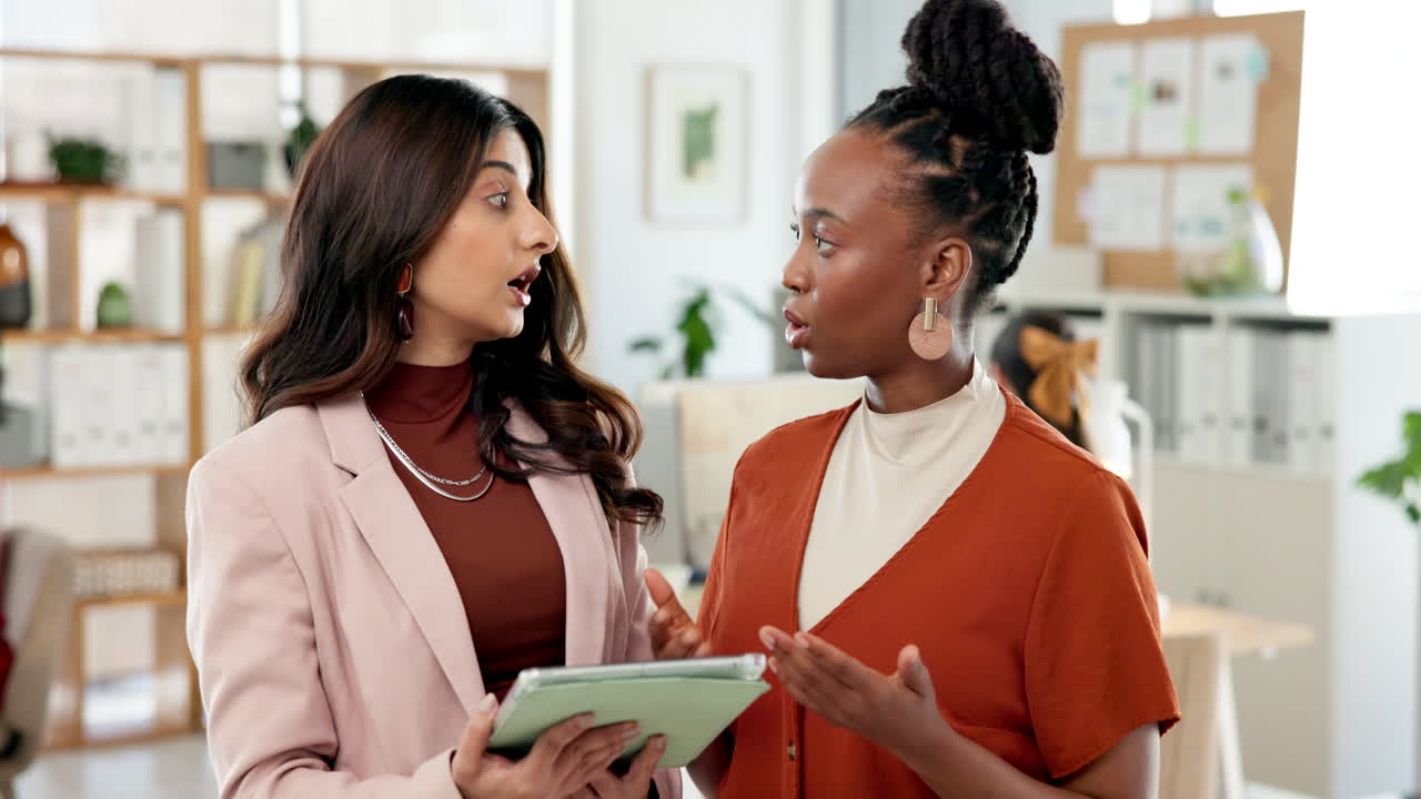 Two Diverse Businesswomen Discussing Work on a Digital Tablet in an Office