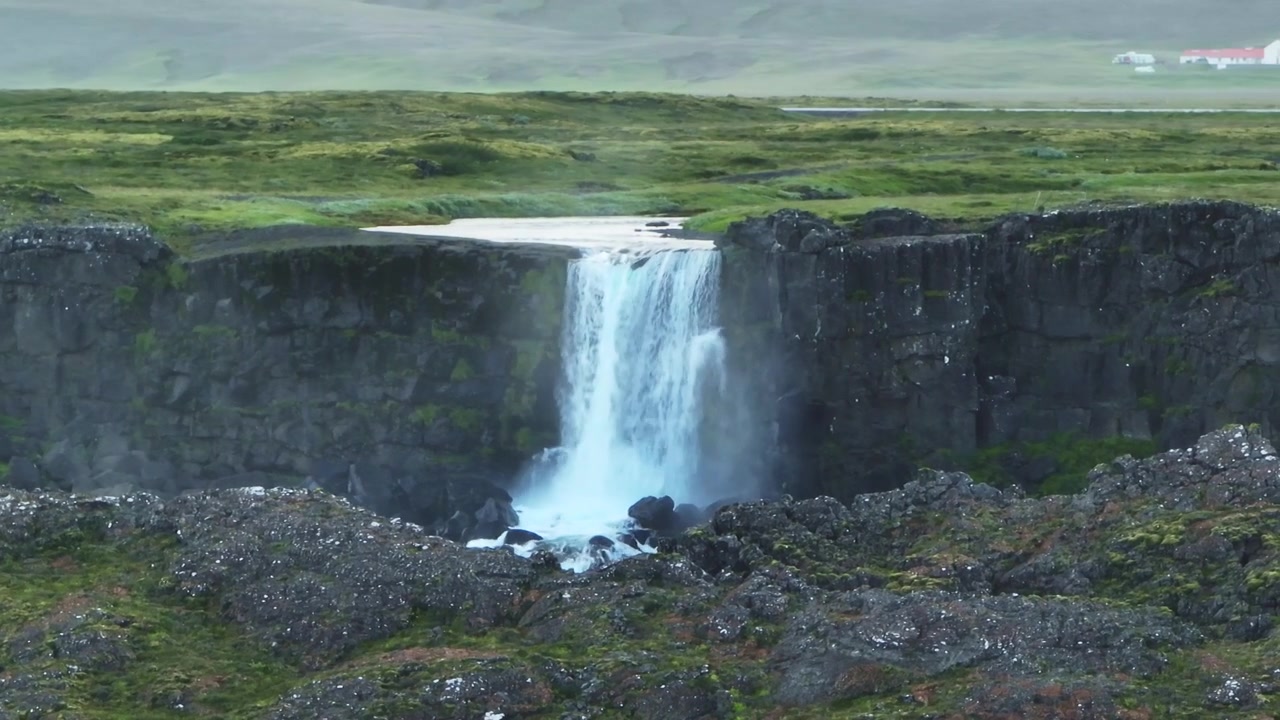 Una vista ravvicinata di una cascata nel Parco Nazionale di Thingvellir, Islanda, circondata da scogliere rocciose e pianure verdi e lussureggianti.