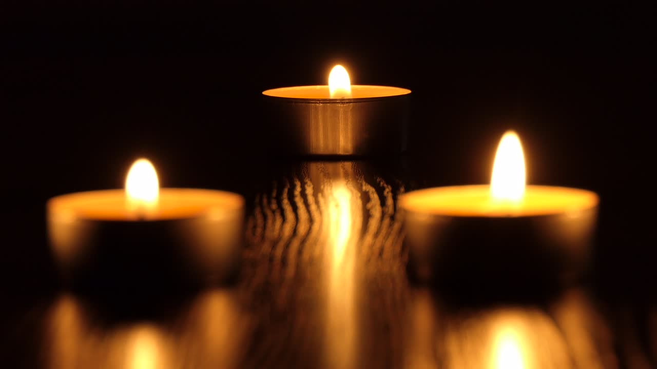 La candela tremola nel buio. Una candela bianca e rotonda brucia su uno sfondo scuro. Candele rotonde bruciano e si spengono. Dolore. Romanticismo. Gioia. Video 4K.