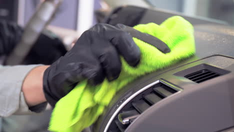 engineer wearing black gloves and using green microfiber cloth to clean up car dashboard