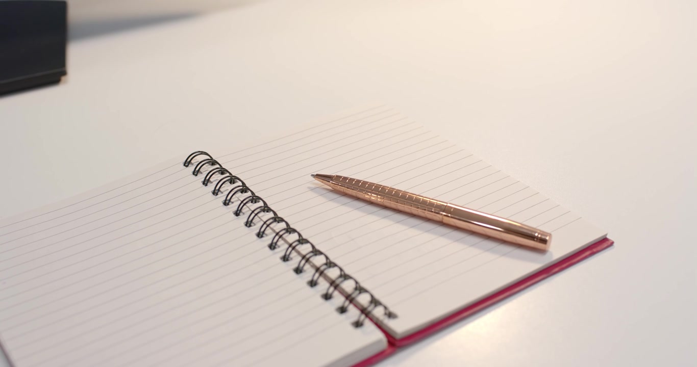 Overhead light is shifting reflections as spiral notebook with rose gold pen is resting on desk