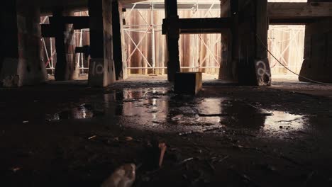 the underside of a ship at a dry dock with water dripping on the floor and wooden posts supported the underside of the ship