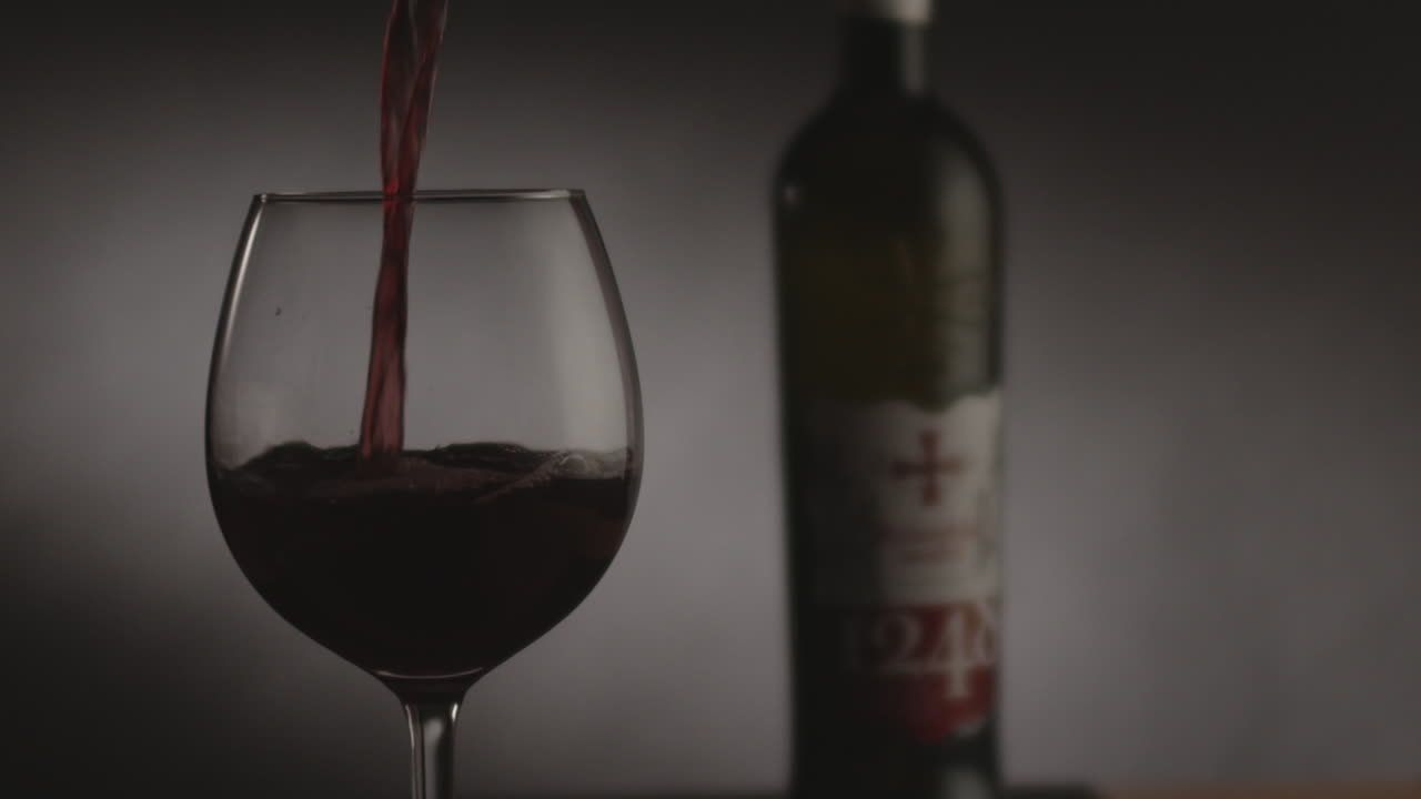 Studio product shot of pouring red wine in to glass on gray background with darker lighting