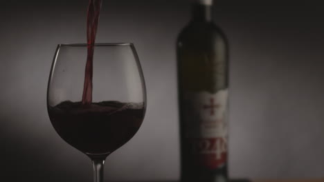 Studio-product-shot-of-pouring-red-wine-in-to-glass-on-gray-background-with-darker-lighting