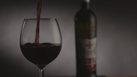 foto de producto de estudio de verter vino tinto en un vaso sobre fondo gris con iluminación más oscura