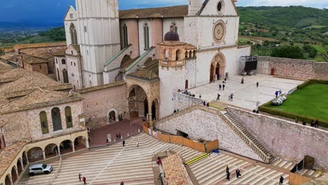 people walking around the portico on the lower plaza and main entrance of basilica of saint francis of assisi in perugia, umbria, italy