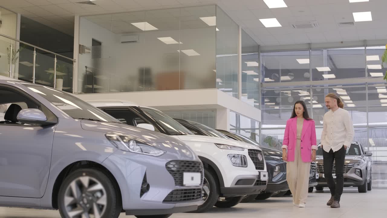 una hermosa pareja de jóvenes en la sala de exposición de automóviles eligiendo un coche nuevo para comprar.