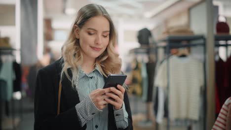 beautiful smiling female customer shopping in clothing store, using smartphone, browsing online, comparing on internet, choosing stylish clothes. fashionable shop, colorful brands, sustainable designs