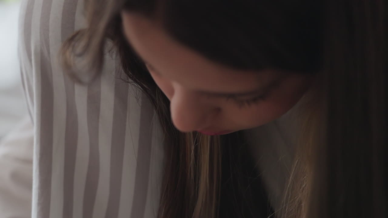 Side view shows elegant girl with head bent, painting toes with black nail polish, soft indoor light, blurred rail background, striped trousers and white sleeve visible, calm focused pedicure moment