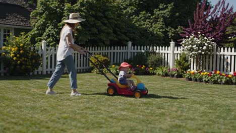 mother pushing a toy lawnmower with her son in the backyard
