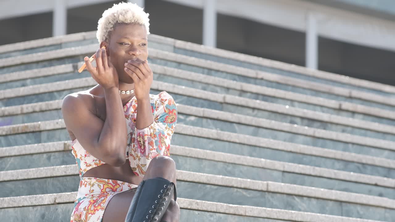 Personne queer noire enthousiaste écoutant un message vocal sur smartphone.