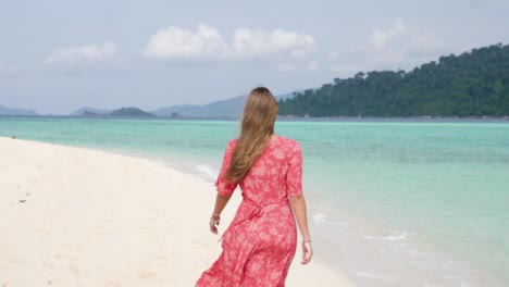 ultra slow motion shot of brunette woman in pink dress walking away from camera on beautiful beach on island in thailand