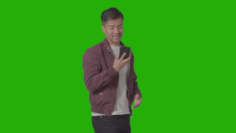 studio shot of smiling casually dressed young man talking on mobile phone against green screen