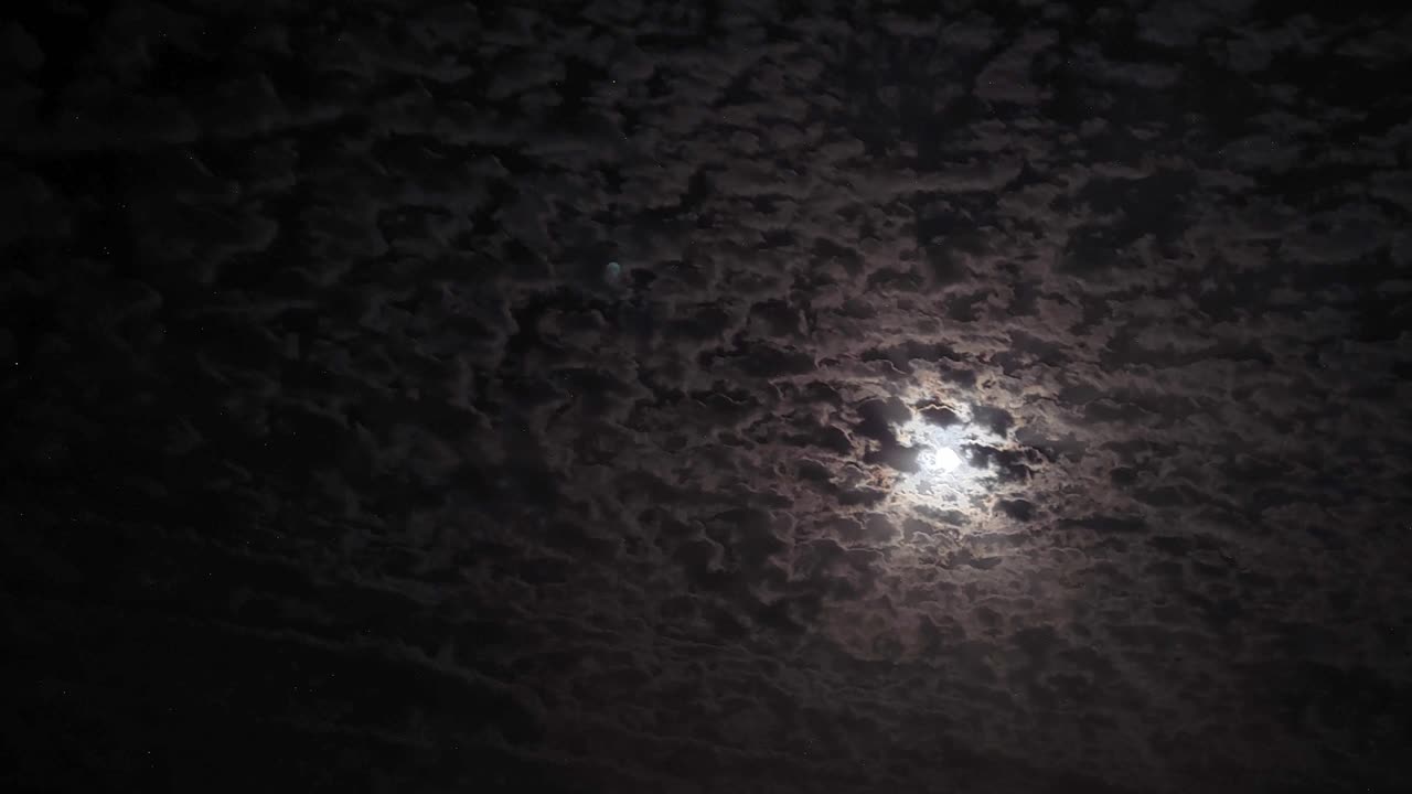 Timelapse. Night sky. Moonlight between fast-moving clouds. Moon and stars between cloud clusters moving across the sky