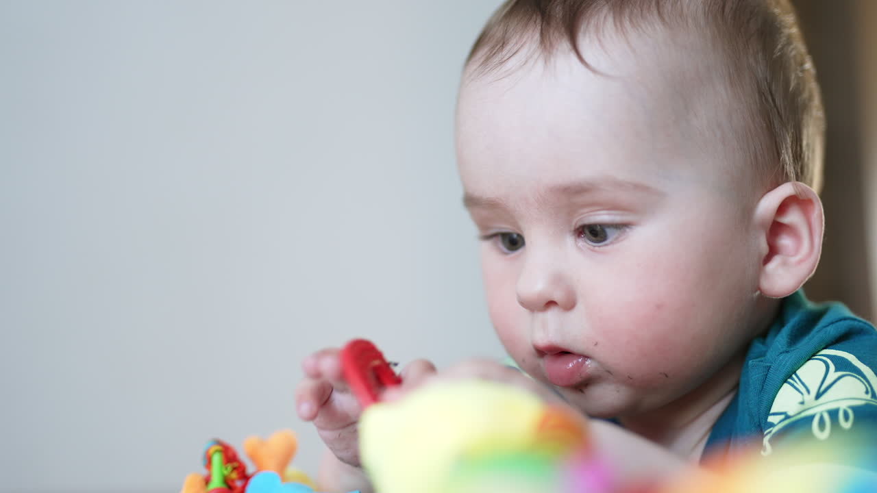 Little adorable baby being busy playing with a toy. Adorable kid totally focused on his toy. Close up. Blurred backdrop.