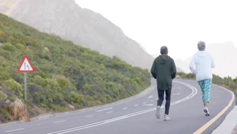 senior biracial couple running together on road in mountains