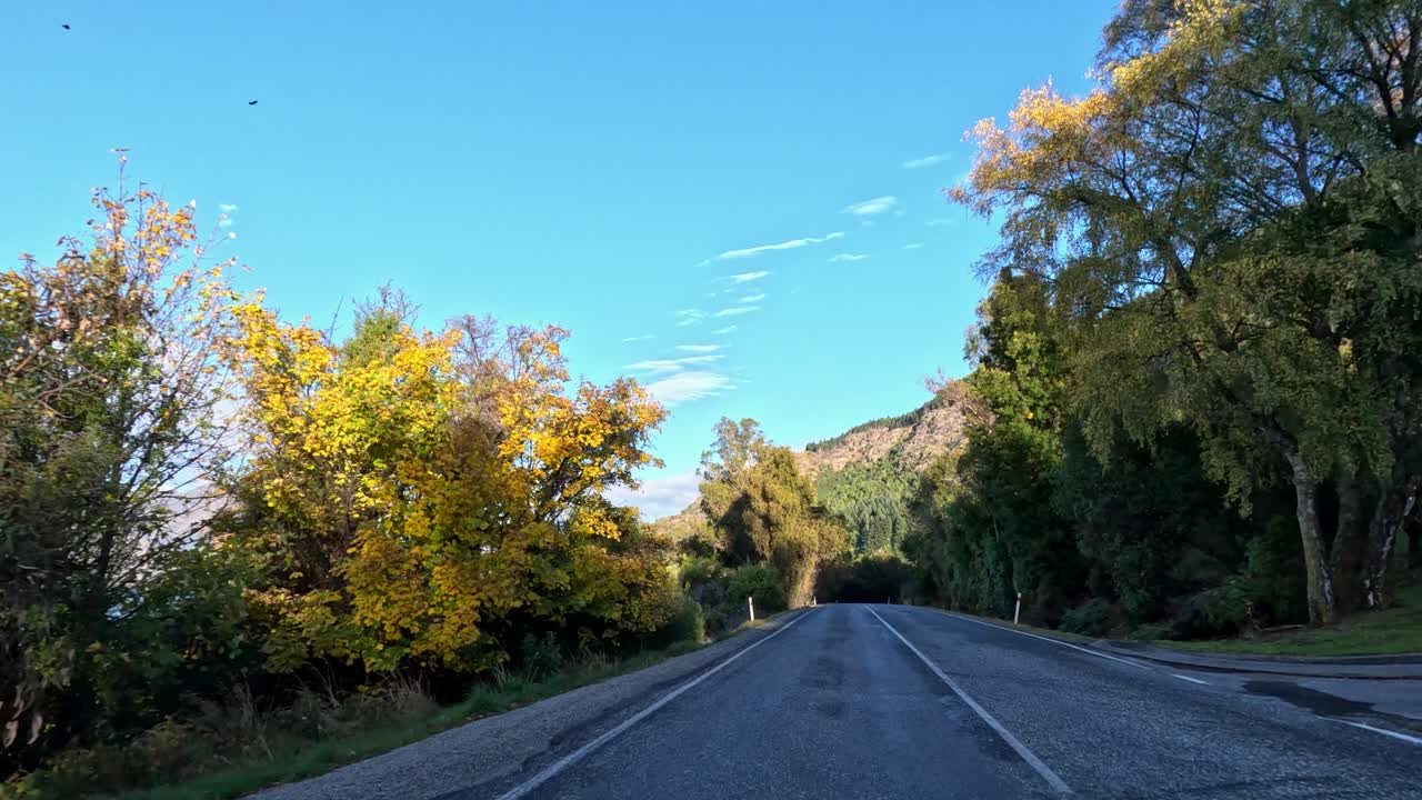 Car drives winding road through autumn foliage, clear skies, mountain landscape, daylight, steady shot