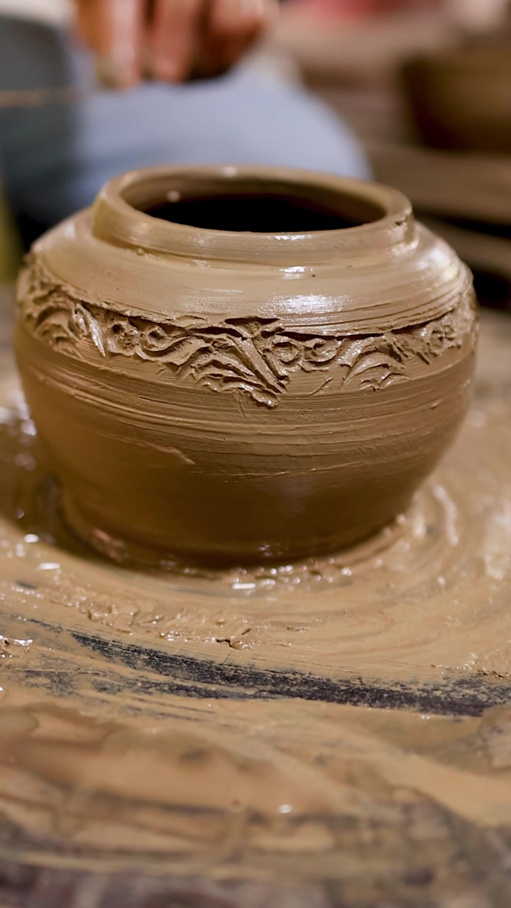 Primo piano di un vasaio che intaglia disegni dettagliati su un vaso di argilla umida in rotazione