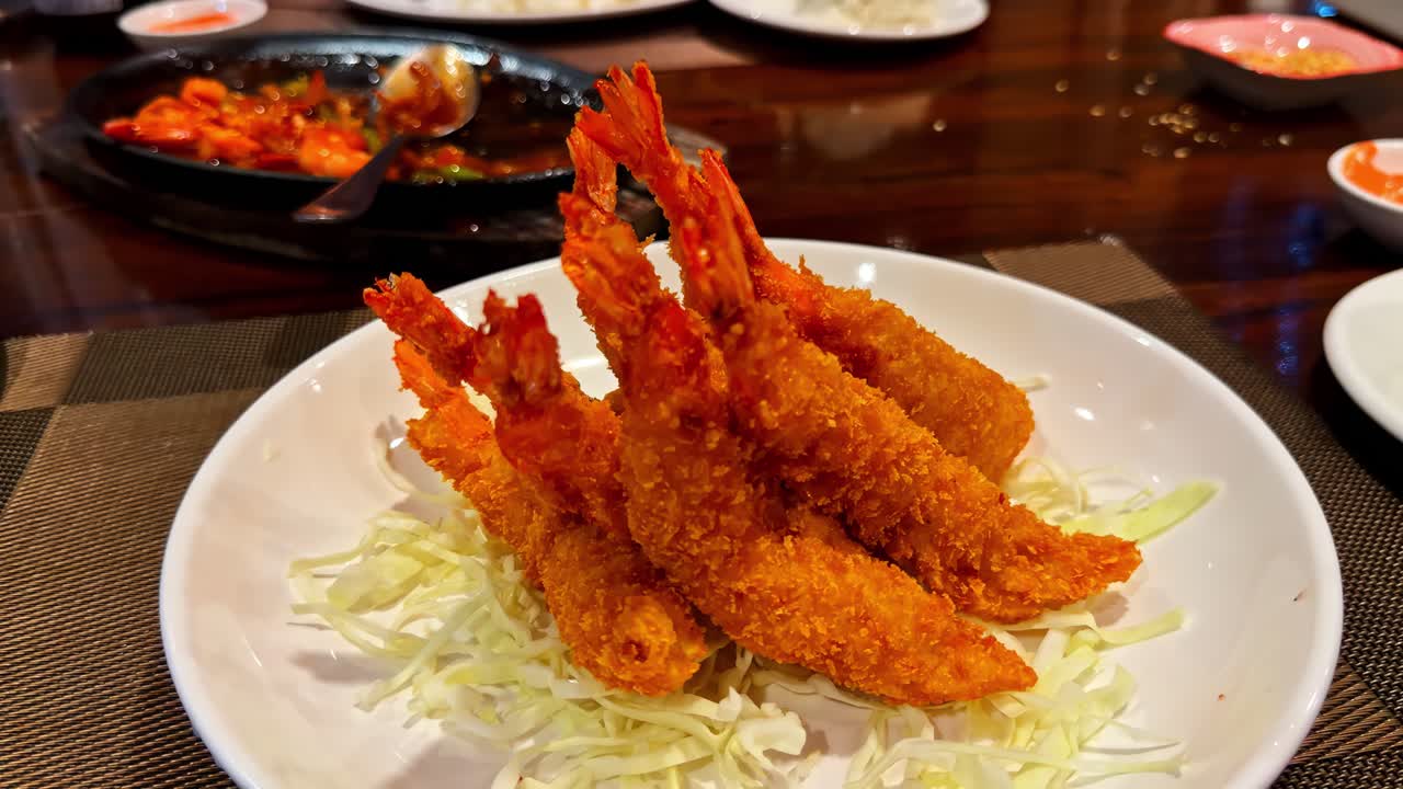 Gamberi impanati croccanti serviti su cavolo cappuccio tritato in una ciotola bianca, che cattura un antipasto di pesce fritto dorato su un tavolo di ristorante.