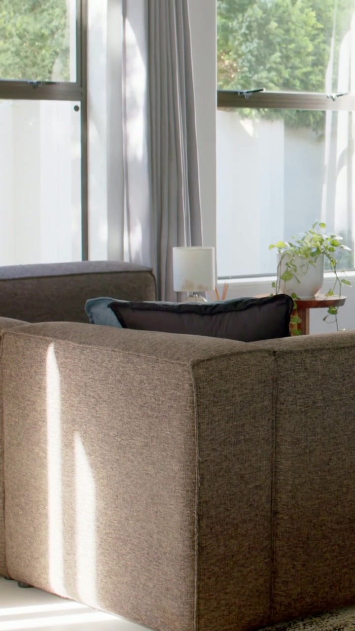Vertical video: Panning camera revealing sofa in home corner to show blue pillow, lamp and window