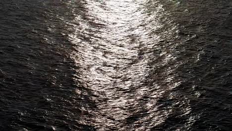 drone push in as light glistens on leathery textured wave ripples on ocean water surface