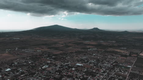 drone video over nopaltepec, mexico, featuring city views, distant mountains, and dark clouds in a rural setting