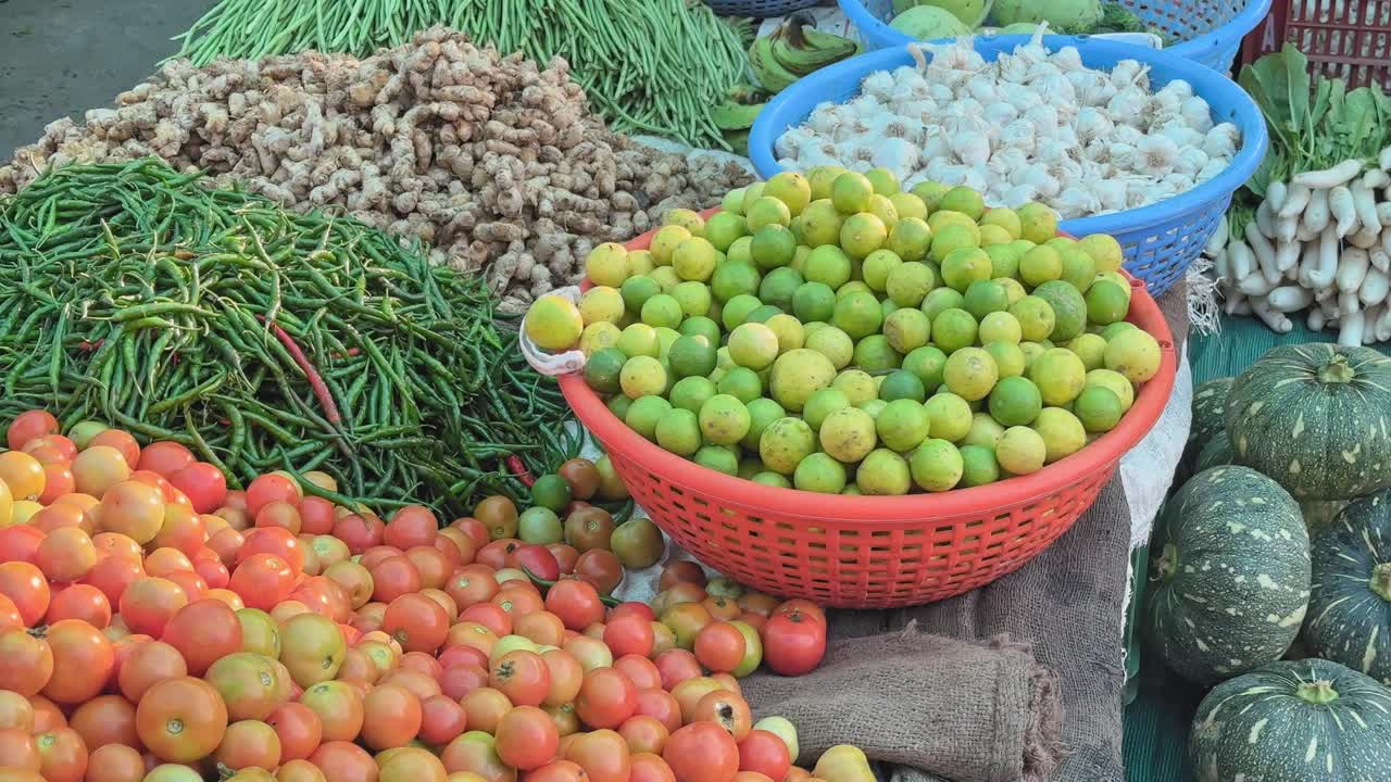 Slow tracking shot over a vibrant market display of tomatoes, lemons, chilies, ginger, and garlic arranged in colorful baskets and piles, showcasing fresh seasonal produce