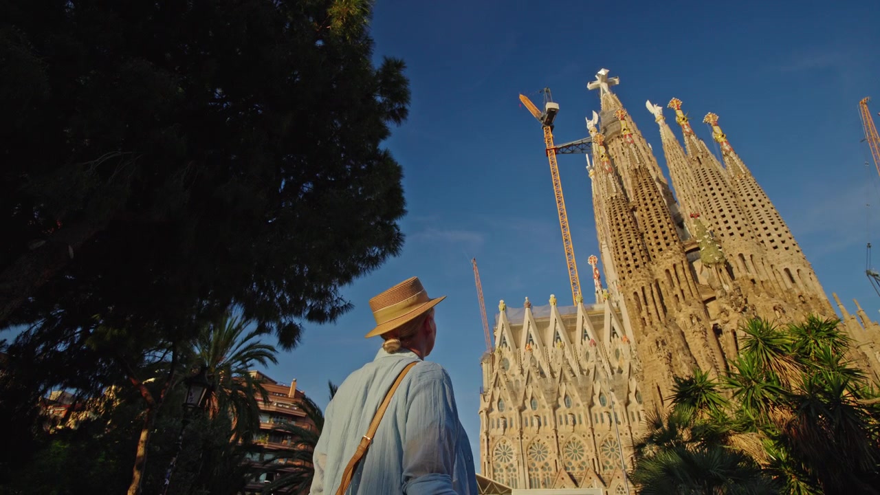 Persona con cappello che ammira la Sagrada Familia a Barcellona in una giornata di sole
