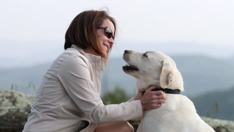 woman pets white lab with mountains in background