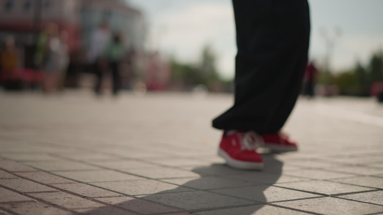 red sneakers crossing open urban plaza with lowangle cinematic framing, blurred crowd in background and long shadow trailing behind, casual stride with light bounce, outdoor city scene in warm