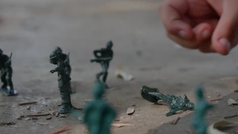 close-up of a child's hands playing with green army men toys in the sand