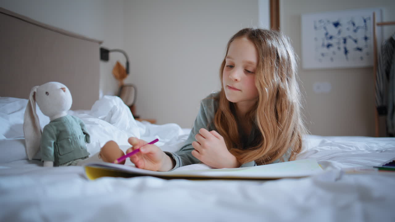 Small child playing toy lying white mattress indoor. Preteen kid drawing pencils