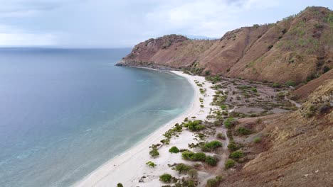 aerial drone rising over dry, arid brown mountainous landscape during dry season with beautiful white sandy beach and ocean views in capital dili, timor leste in southeast asia