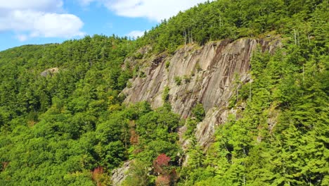 Luftaufnahmen-Drängen-In-Richtung-Einer-Bewaldeten-Klippe-Mit-Einem-Einsamen-Kletterer-In-Blau