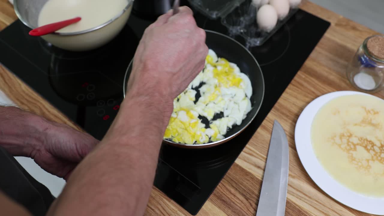 Person cooking scrambled eggs in a kitchen