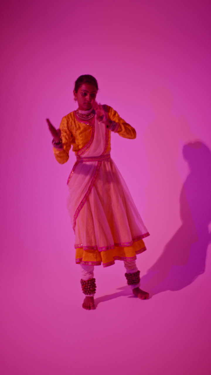 video vertical de longitud completa de estudio de una bailarina de kathak que realiza un baile vestida con el vestido tradicional indio contra un fondo púrpura